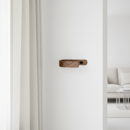 Wooden curtain holdback with black fittings on a white wall with a blurred living room in the background